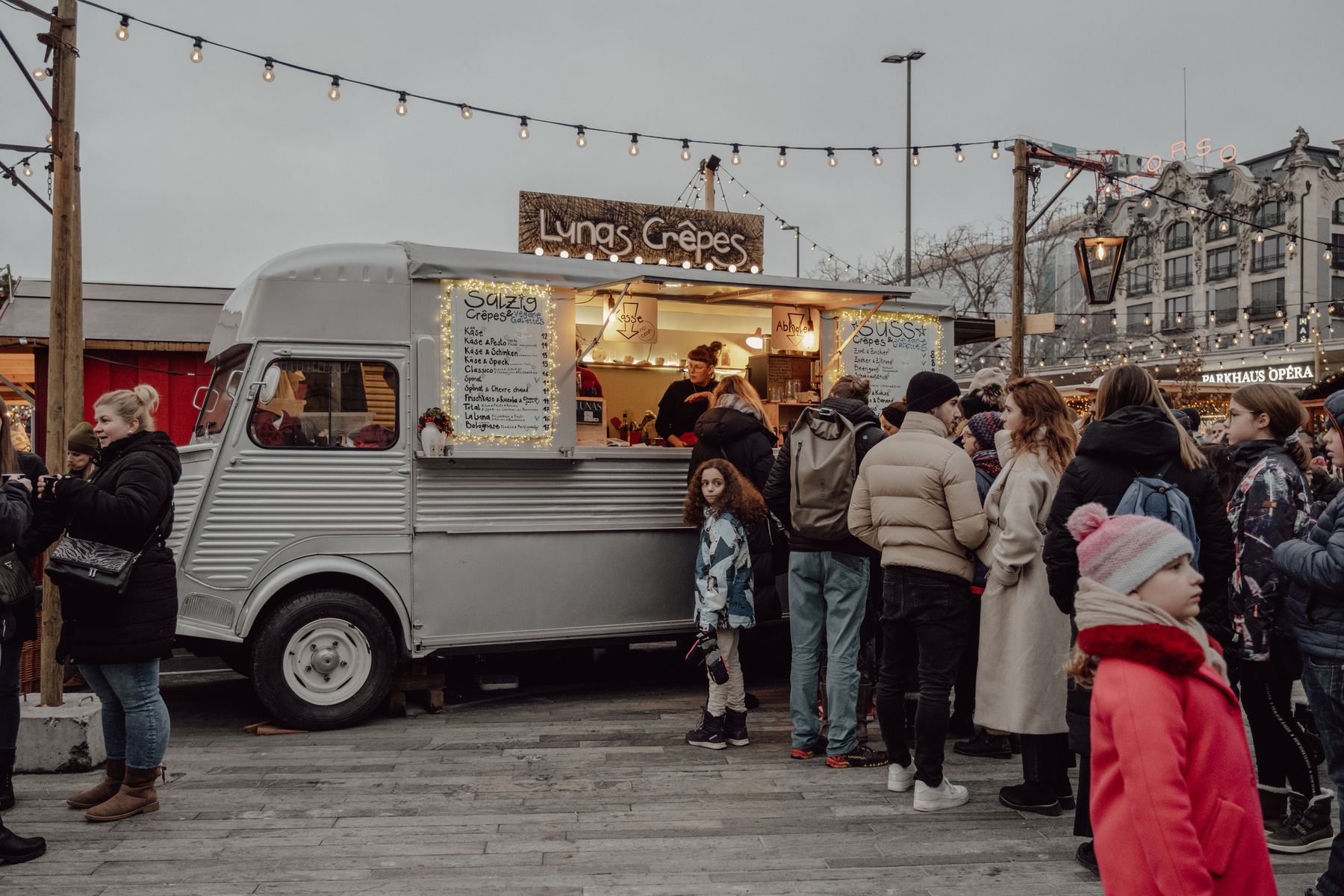 A queue of customers at a food truck serving crêpes at an outdoor market.
